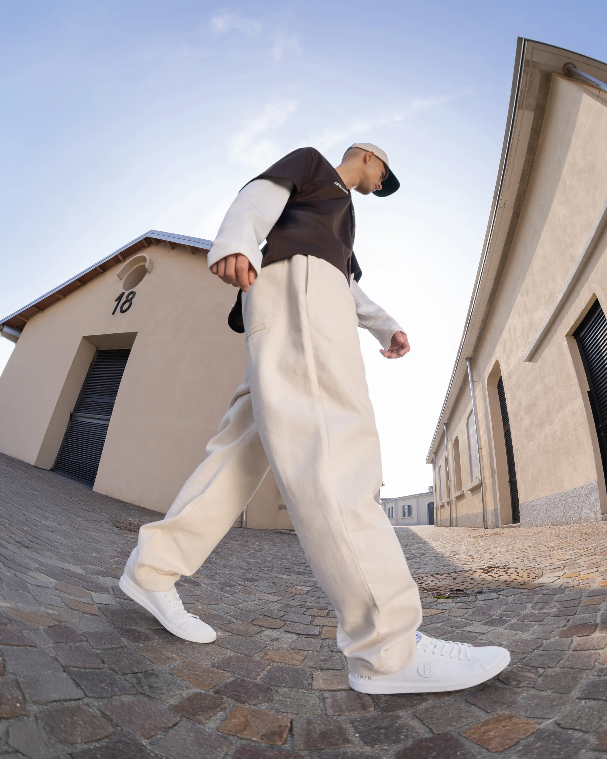 Close-up of white Cotton Belt sneakers worn by a man walking.